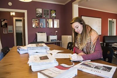 female student in a sweater and scarf at the rose oneill literary house, writing surrounded by event posters and publications
